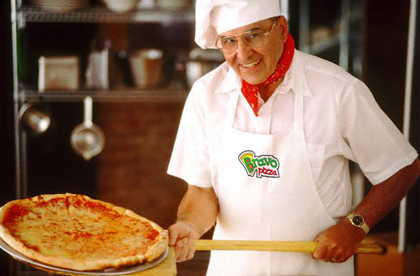 Повар пиццерии «Пицца Браво» в белоснежном корпоративном фартуке с нанесенным на него логотипом